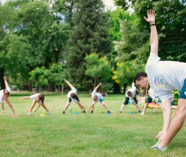 Kids stretching exercises in a park guided by a coach, promoting fitness and fun.