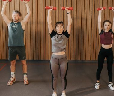Three adults exercising with dumbbells in a gym setting, promoting fitness and healthy lifestyle.
